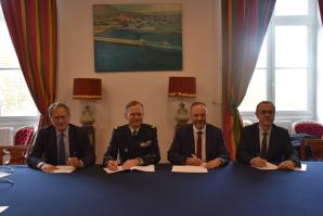 4 hommes de face (dont un en costume d'officier) en train de signer un document