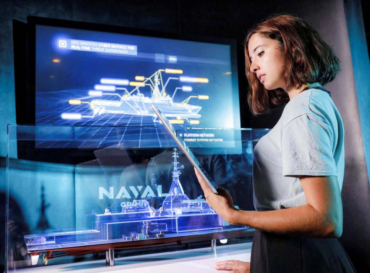 Estelle Hotellier devant un écran de la cybersécurité et une maquette de la FDI